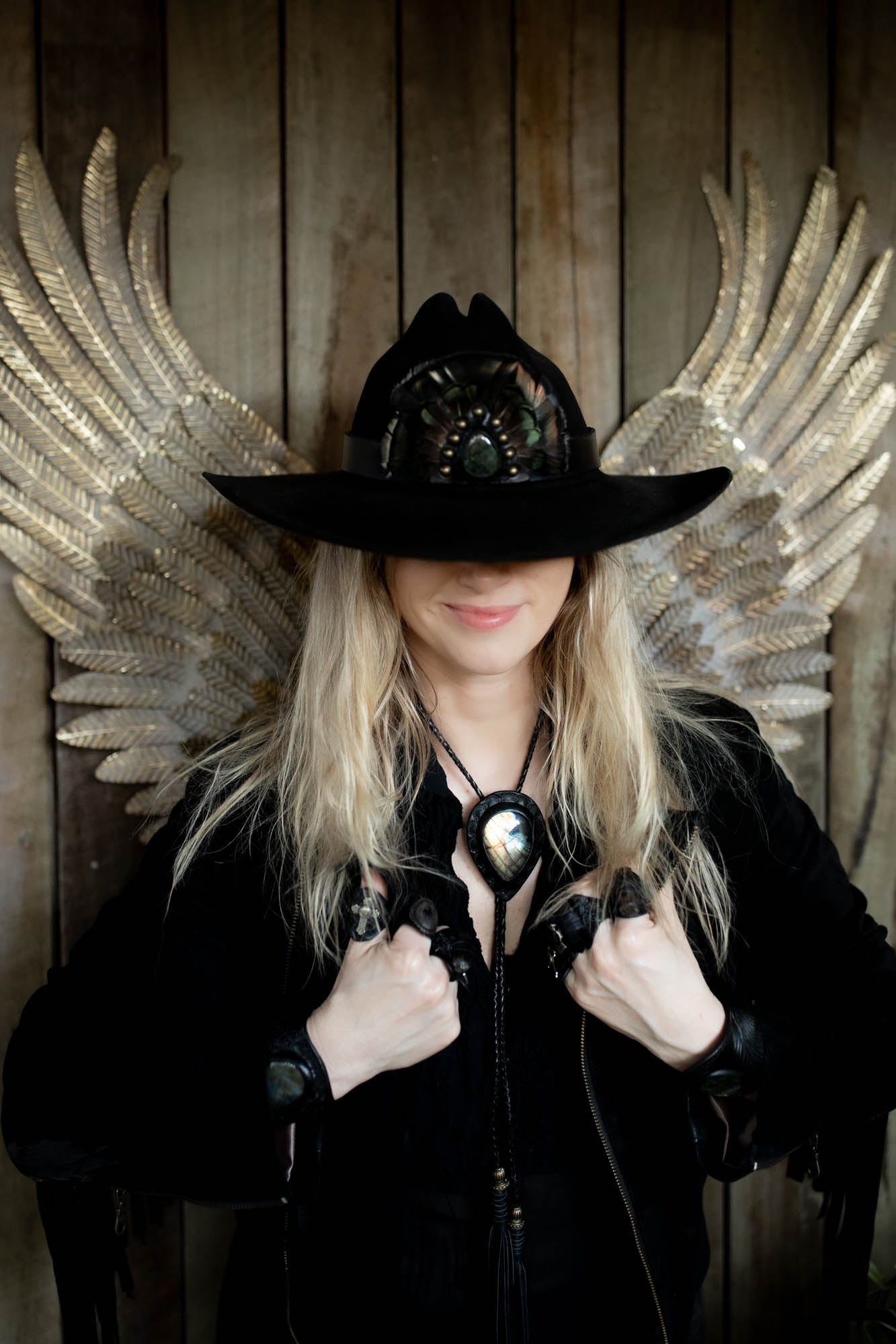 Person wearing a black hat with decorative wings against a wooden background