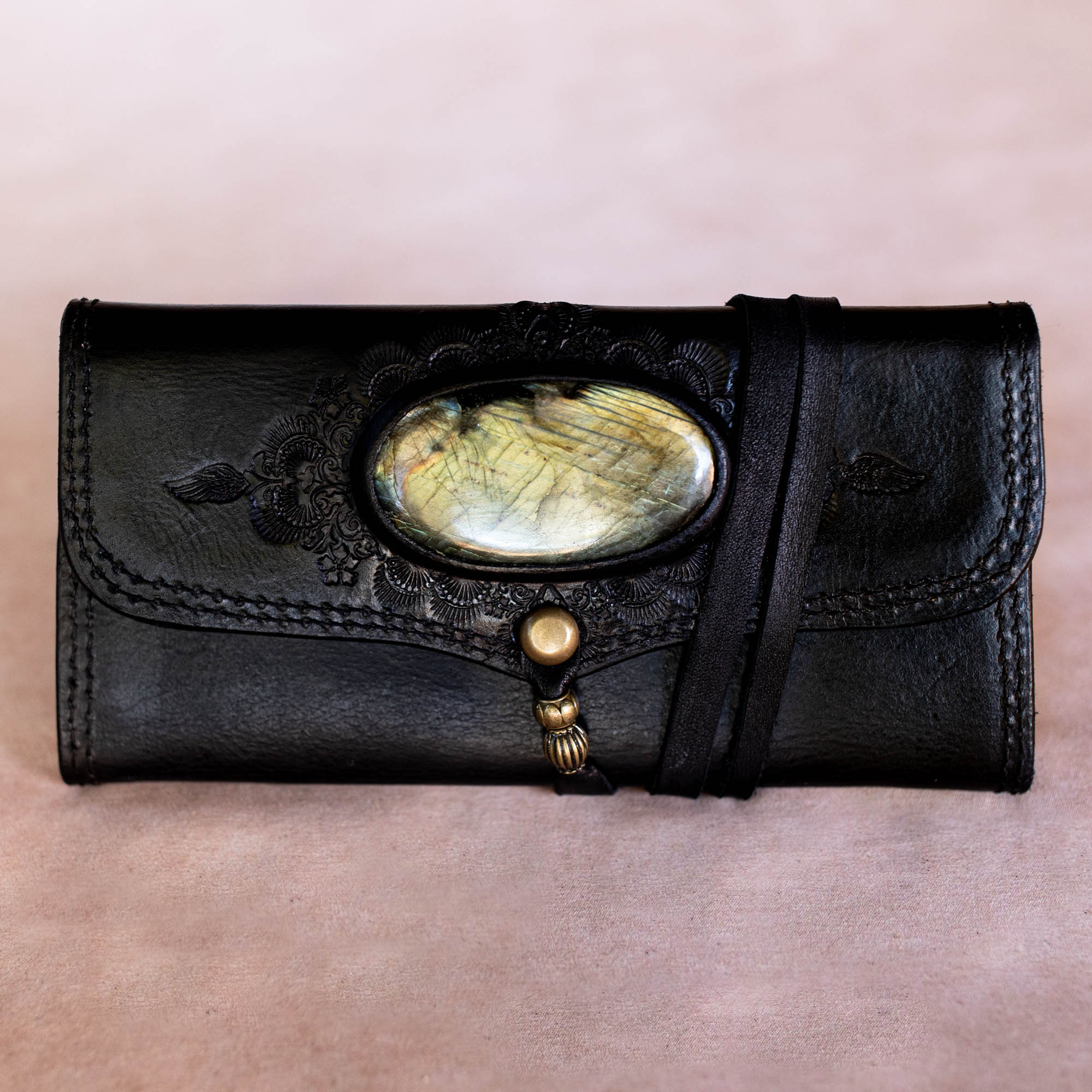 Black leather clutch with decorative stone and button on a beige background