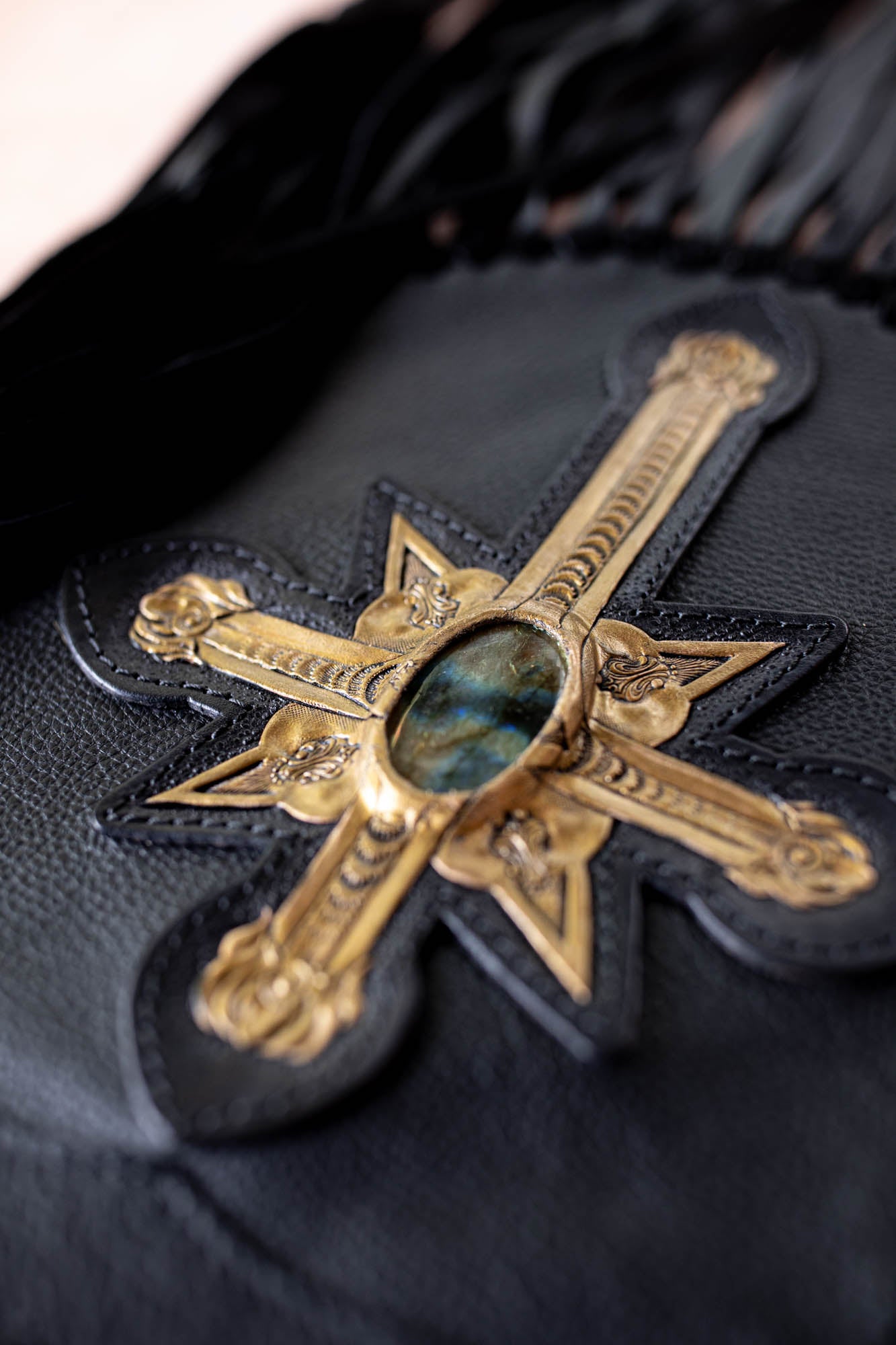 Decorative gold cross with gemstone on a black leather surface