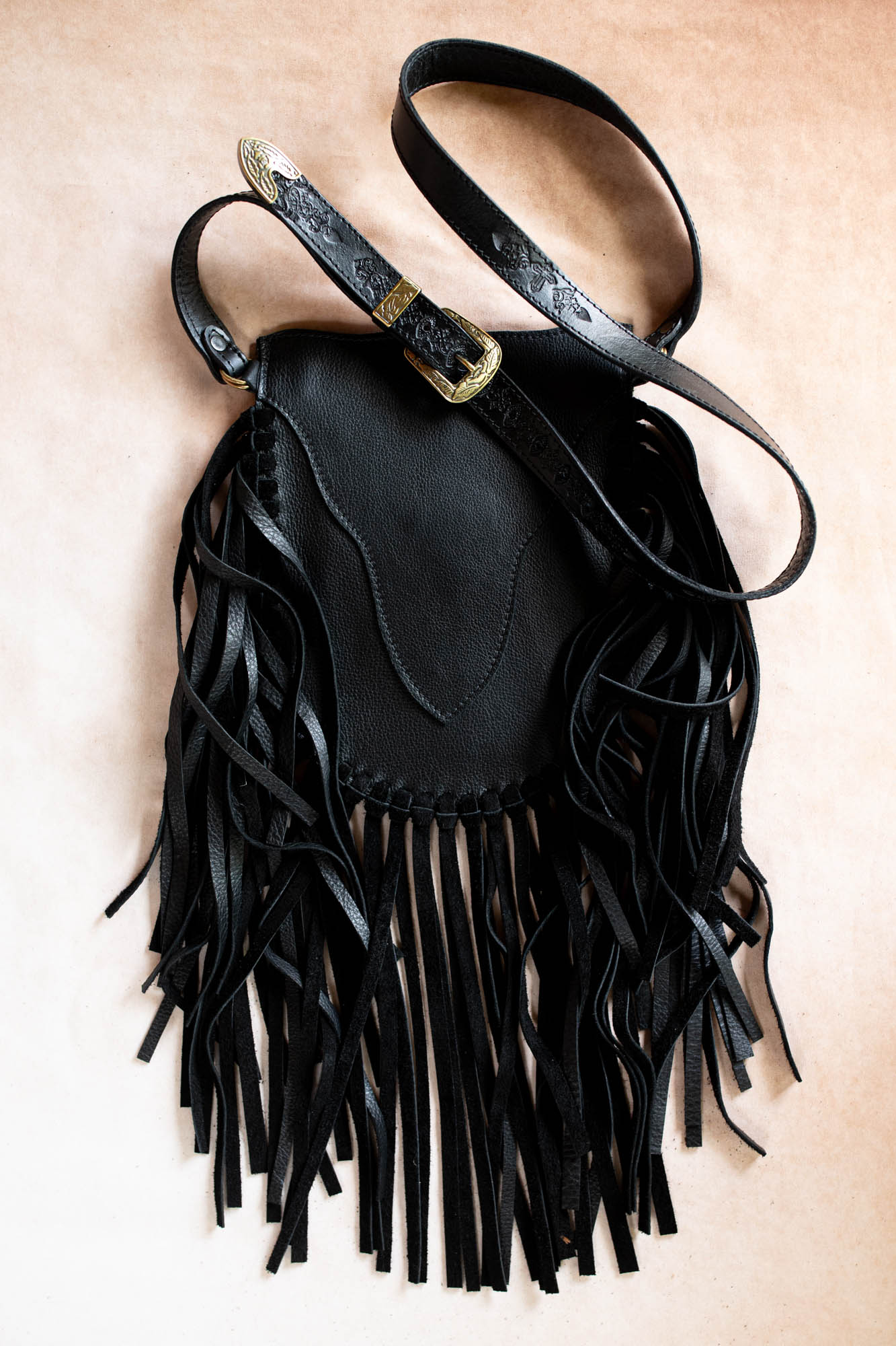 Black leather handbag with fringe details on a beige background
