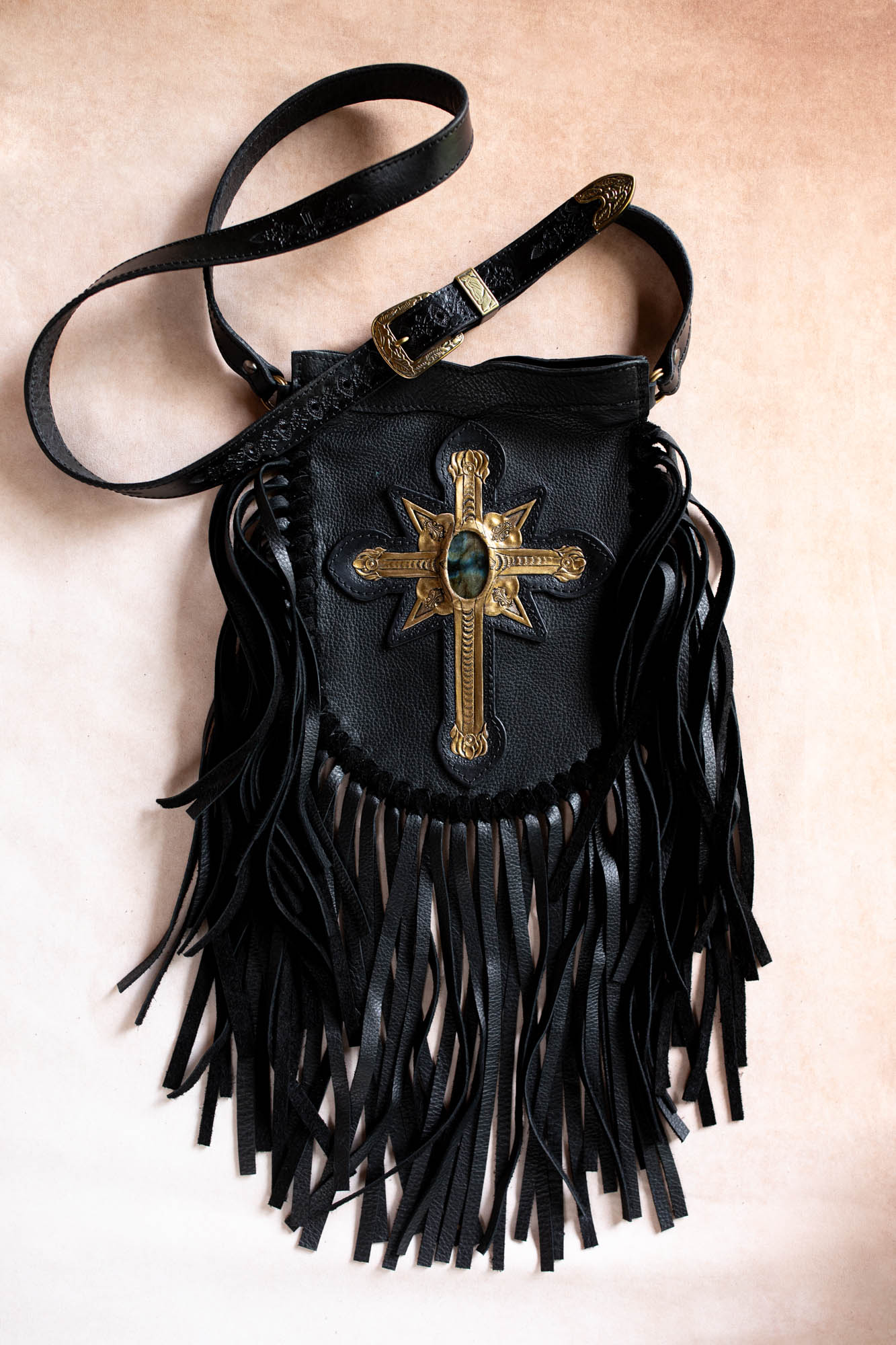 Black fringe bag with gold emblem on a beige background